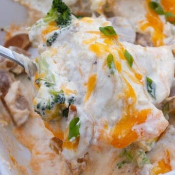 A spoonful of cheesy broccoli casserole with mushrooms and green onions in a baking dish.