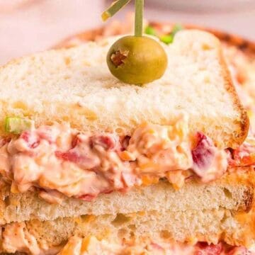Close-up of a stacked pimento cheese sandwich garnished with a green olive on top.