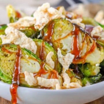 A bowl of roasted Brussels sprouts topped with crispy bits and drizzled with a red sauce.