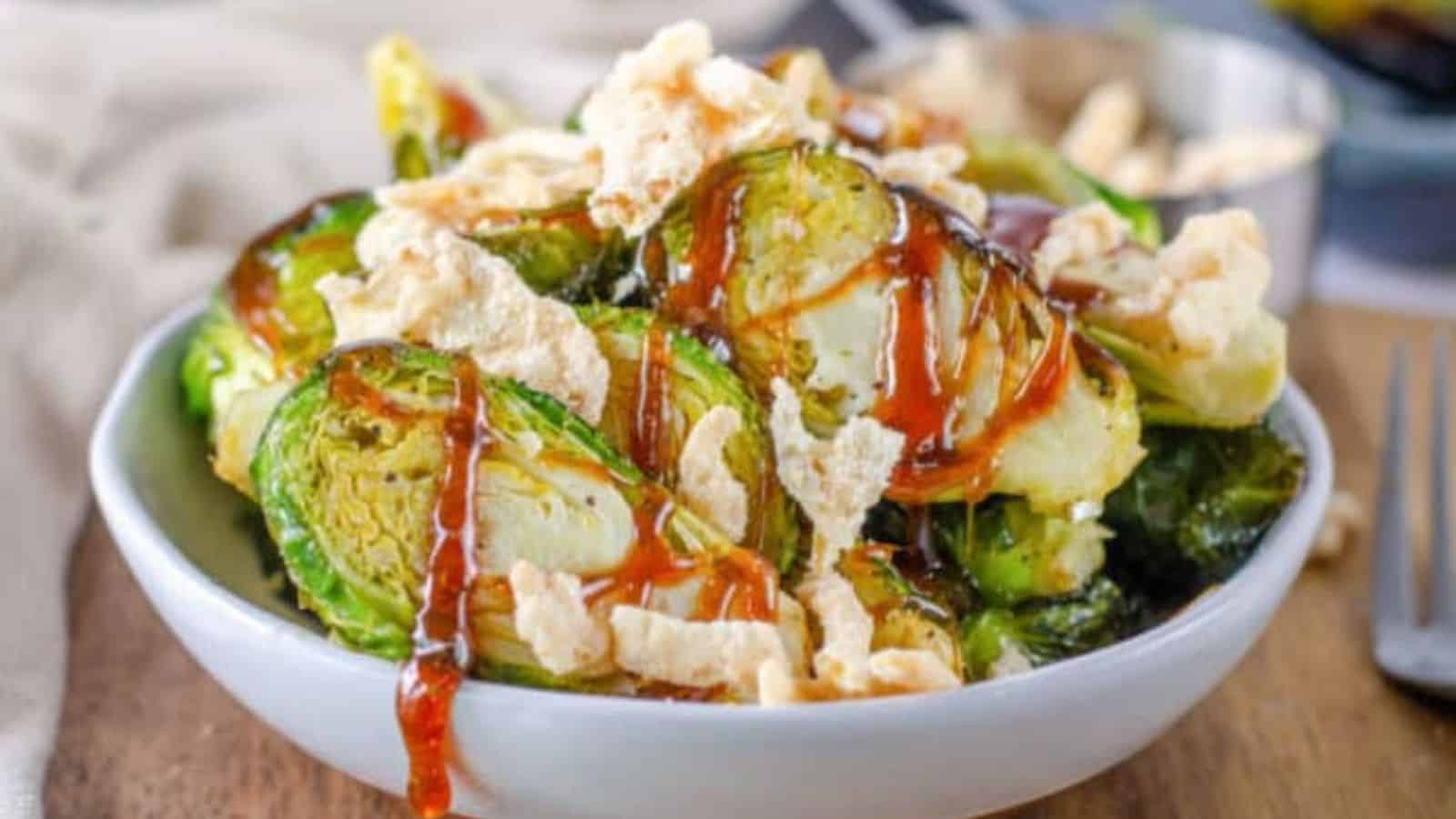A bowl of roasted Brussels sprouts topped with crispy bits and drizzled with a red sauce.