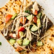 Grilled flatbread topped with kebab, chopped cucumber, tomato, onions, and drizzled with sauce.