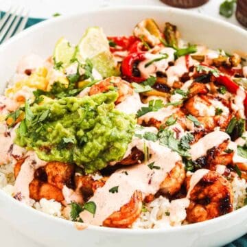A burrito bowl with rice, grilled chicken, guacamole, veggies, sauce, and cilantro in a white bowl.