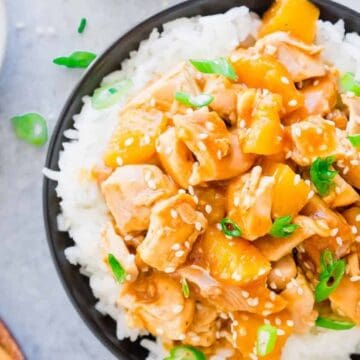 A bowl of white rice topped with teriyaki chicken, pineapple chunks, sesame seeds, and chopped green onions.