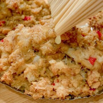 Close-up of chopsticks holding crispy fried oyster omelette with red chili pieces on a metal tray.
