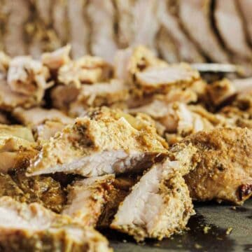 Close-up of sliced, seasoned roasted meat with onions on a dark surface.