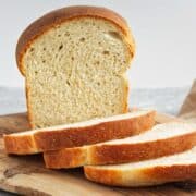 A loaf of bread with several slices cut, displayed on a wooden cutting board.
