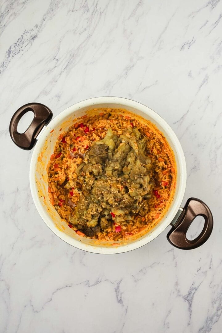 A pot of jollof rice topped with stewed meat and sauce on a marble countertop.