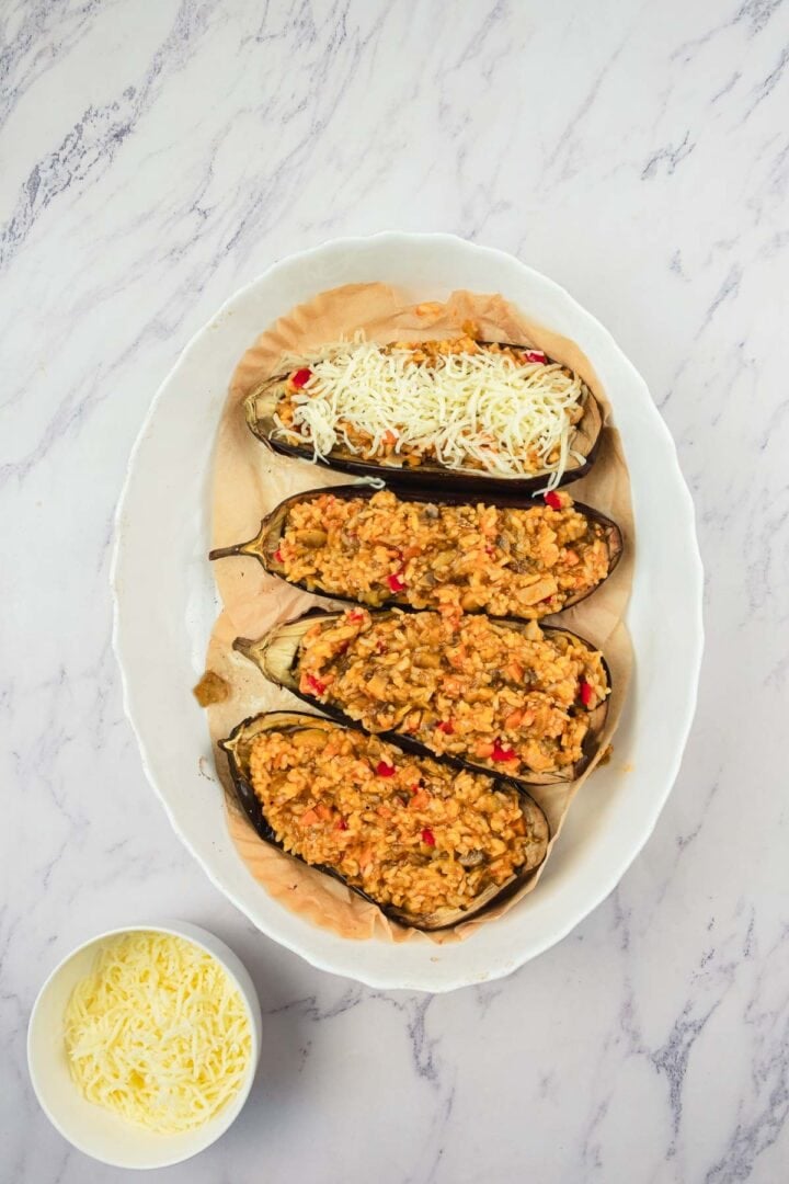 Four eggplant halves stuffed with a vegetable mixture, three topped with cheese, on a white oval plate.