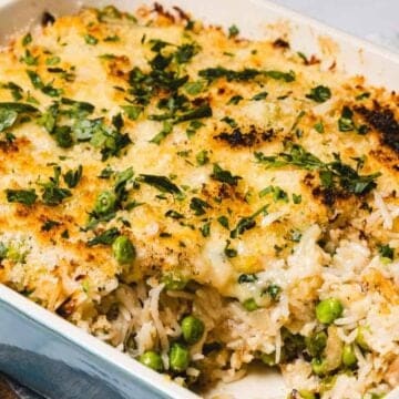 A baked casserole topped with melted cheese and herbs, with rice and green peas visible inside.
