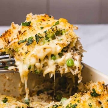 A spatula lifts a cheesy, baked casserole with peas and herbs from a baking dish.