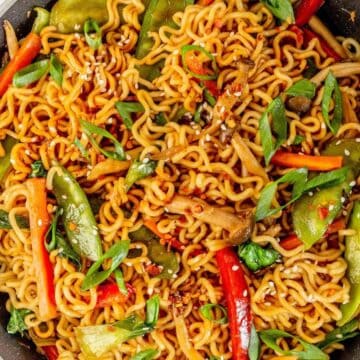 A pan filled with stir-fried noodles, snap peas, bell peppers, mushrooms, and garnished with green onions.