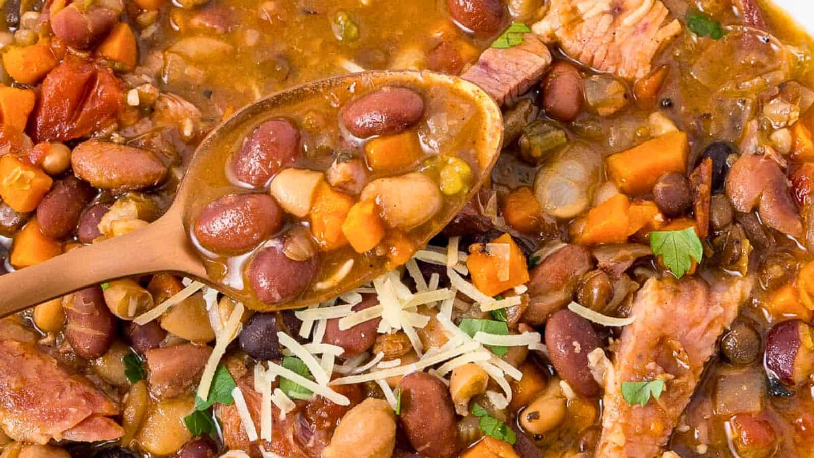 A close-up of bean and vegetable soup with shredded cheese and herbs, a spoon resting in the bowl.