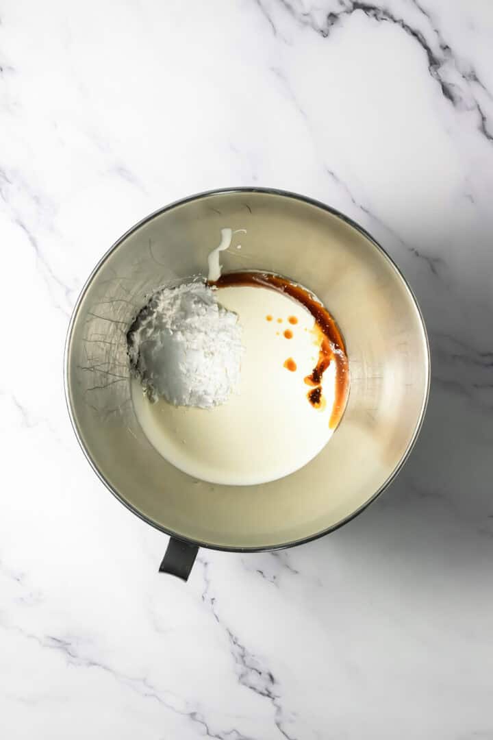 Metal mixing bowl with cream, powdered sugar, and vanilla on a white marble surface&mdash;perfect beginnings for a luscious chocolate mousse.