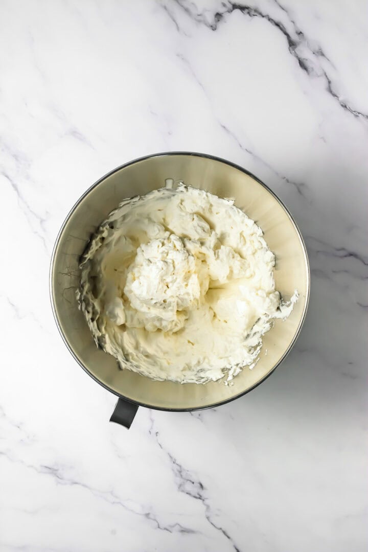 A mixing bowl filled with creamy, whipped chocolate mousse sits on a white marble surface.