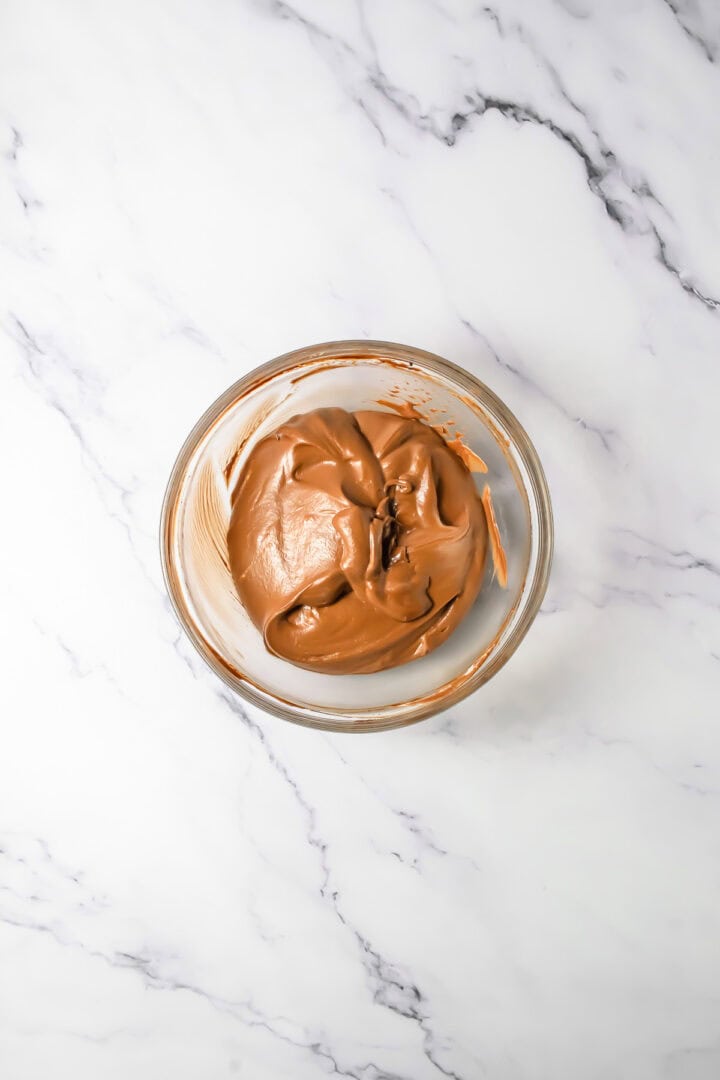 A glass bowl with creamy Chocolate Mousse mixture sits on a white marble surface.