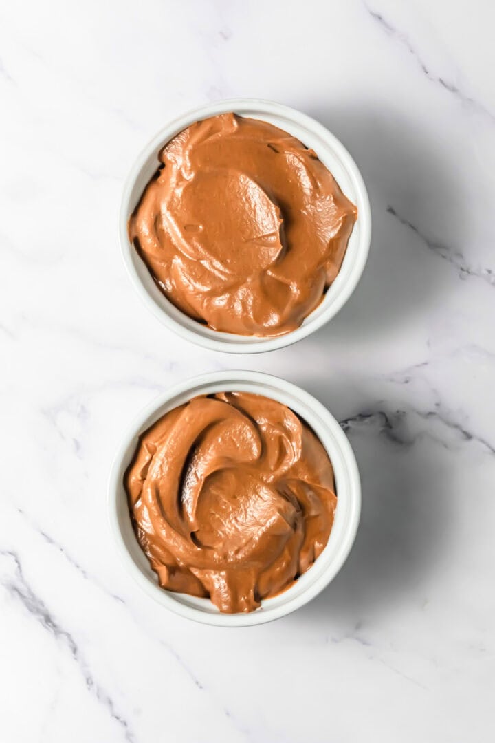 Two white ramekins filled with rich, creamy Chocolate Mousse sit on a white marble surface.
