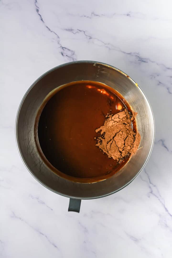 A metal mixing bowl with cocoa powder and wet chocolate batter on a white marble surface.