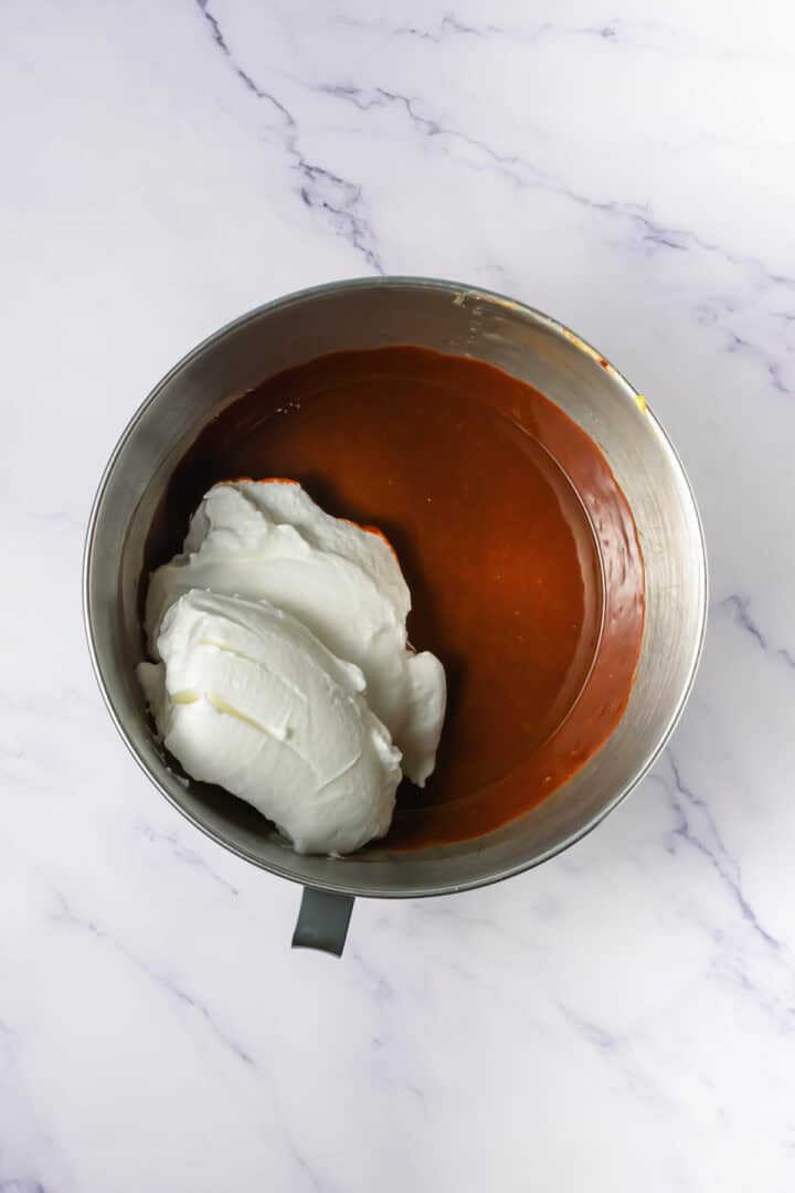 A mixing bowl with chocolate batter and a large dollop of whipped egg whites on a marble surface.