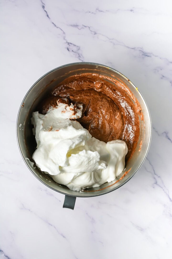 A mixing bowl with chocolate batter and fluffy whipped egg whites on a marble countertop.