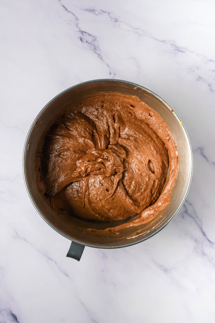 Mixing bowl filled with smooth chocolate cake batter on a white marble surface.