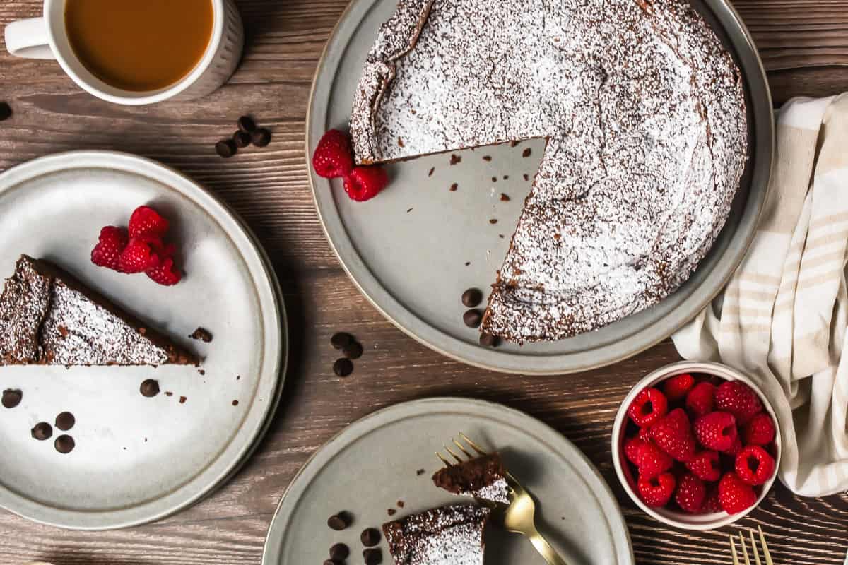 Chocolate cake with powdered sugar, raspberries, coffee, and gold forks on a wooden table.