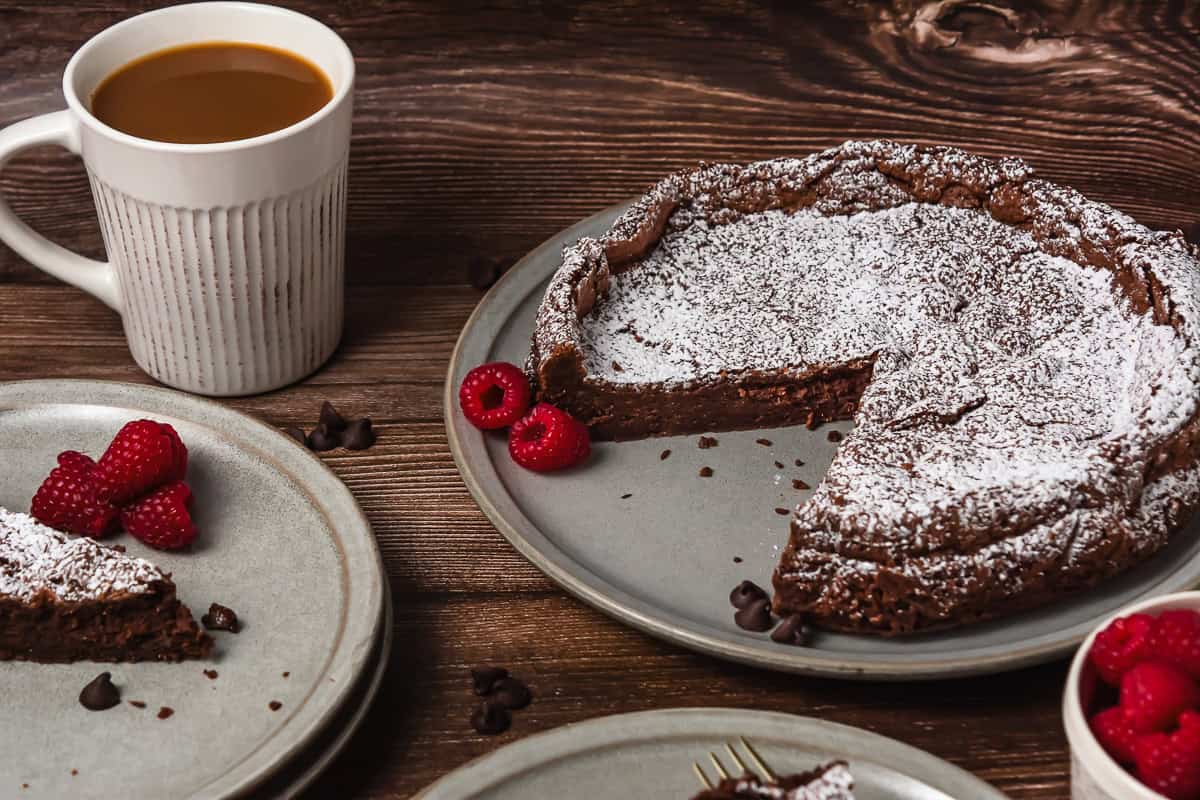 Chocolate cake with powdered sugar, raspberries, and coffee on rustic plates and a wooden table.