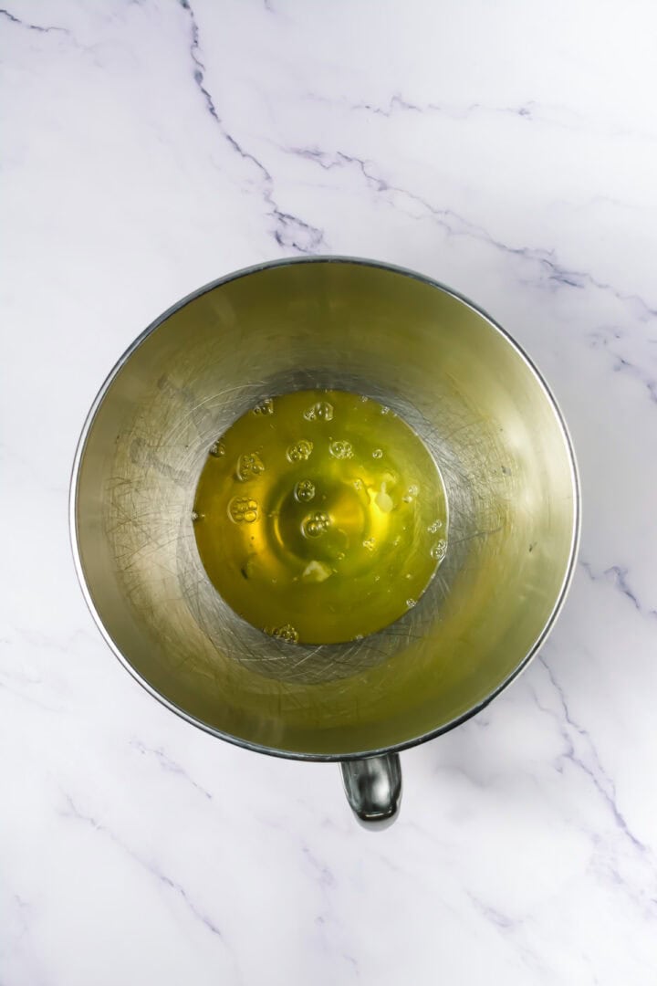 Overhead view of egg whites in a metal mixing bowl on a white marble countertop.