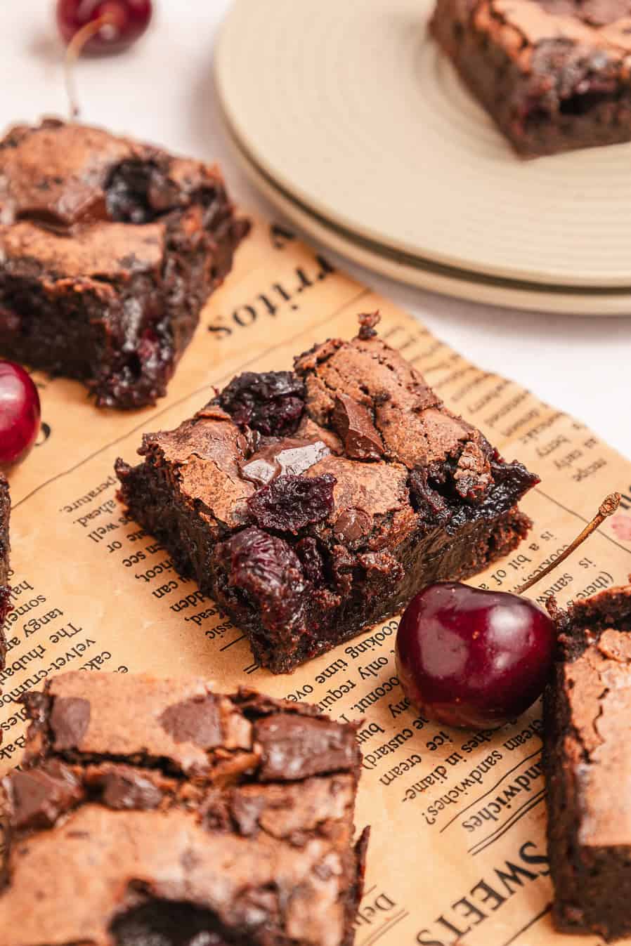 Fudgy chocolate cherry brownies on parchment paper with fresh cherries beside them.