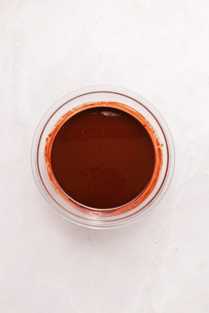A glass bowl filled with smooth, melted chocolate on a white marble surface.