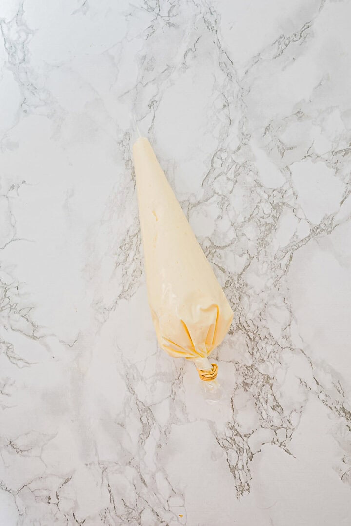 A piping bag filled with cream cheese mixture on a marble countertop.