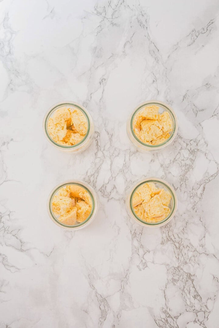 Four small glass jars filled with yellow ice cream on a white marble surface, arranged in a square.
