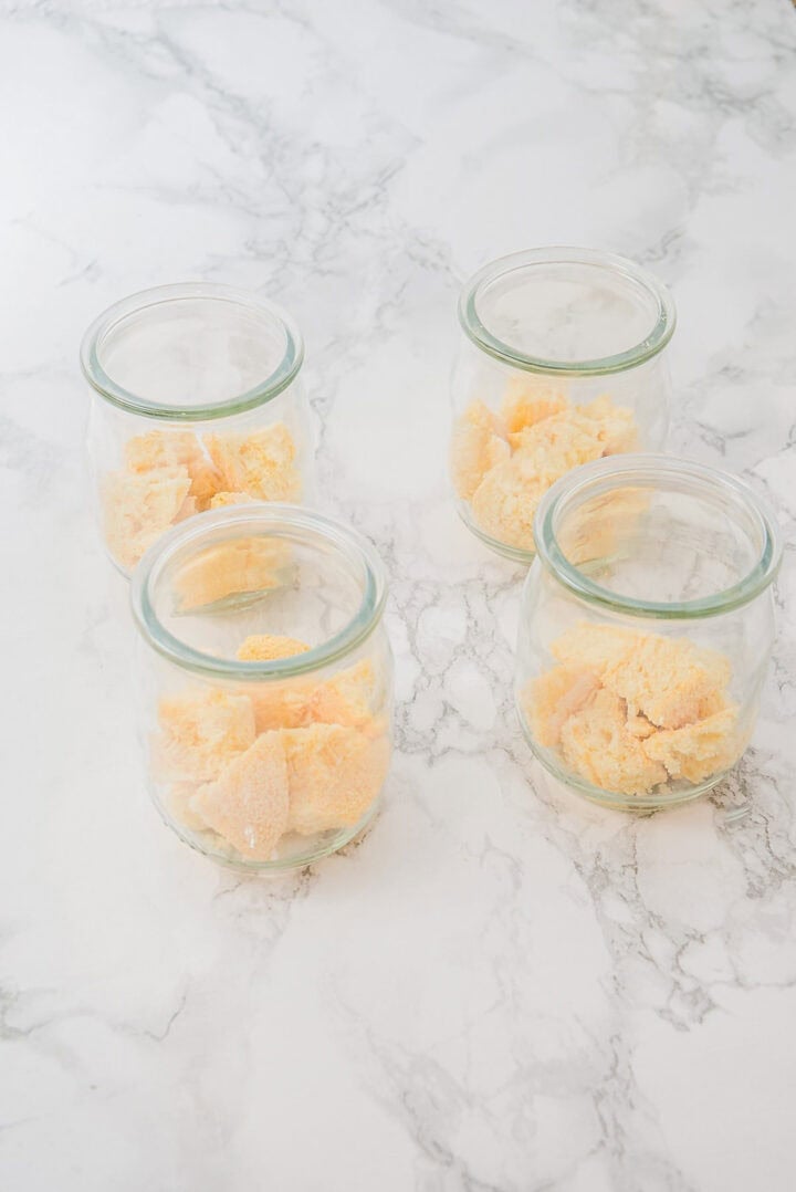 Four glass jars partially filled with scoops of yellow ice cream on a marble surface.