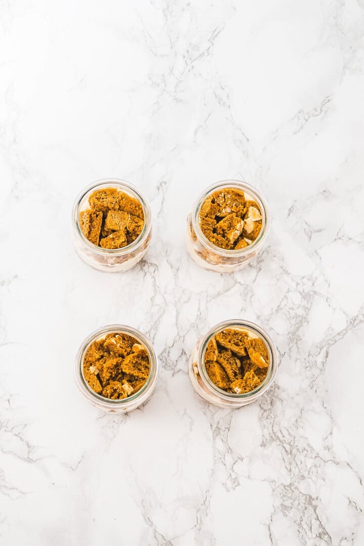 Four small glass jars filled with crumbled cookies on a white marble surface, arranged in a square.