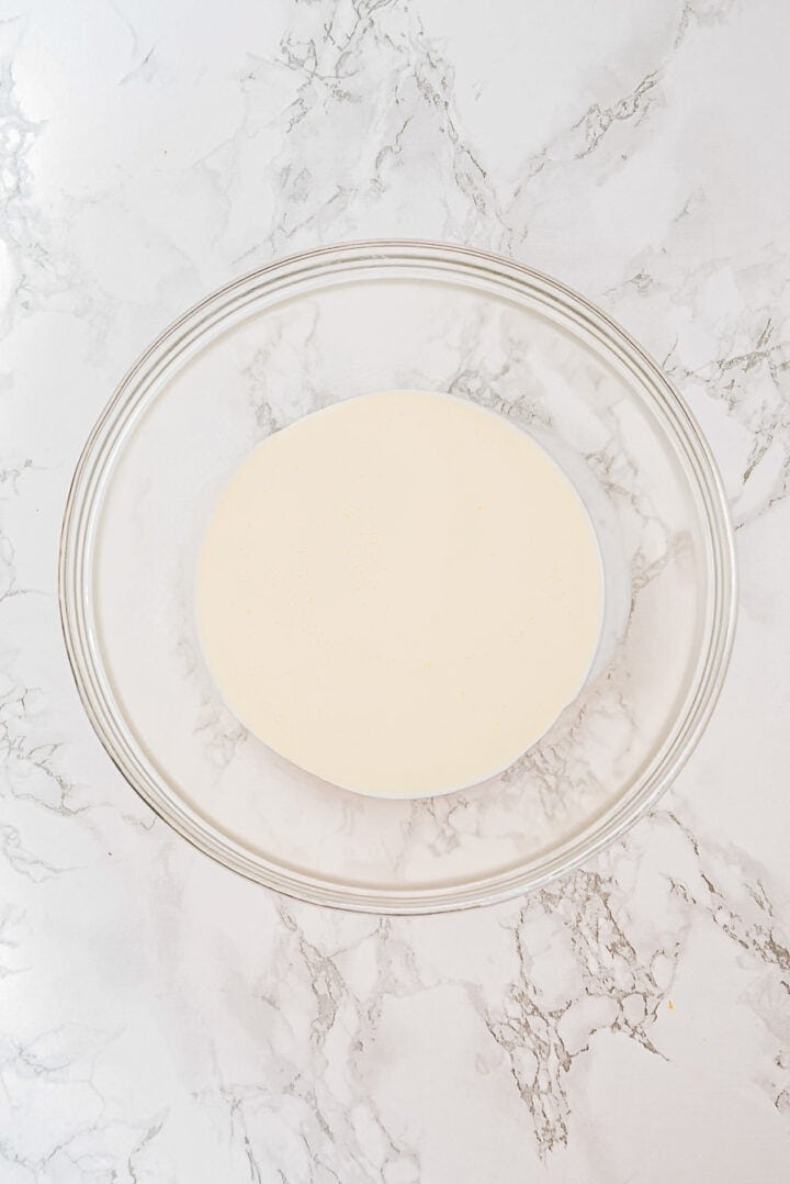 A glass bowl with a smooth, pale batter on a white marble surface.