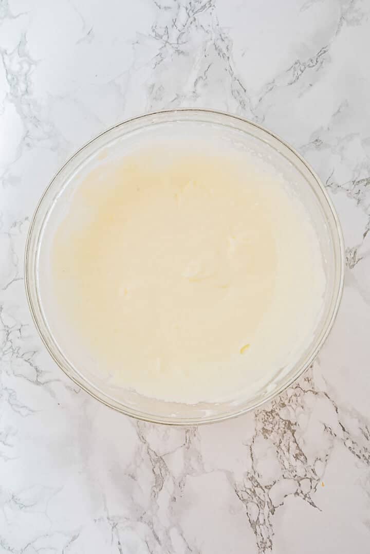 A glass bowl filled with creamy, pale batter sits on a white marble surface.