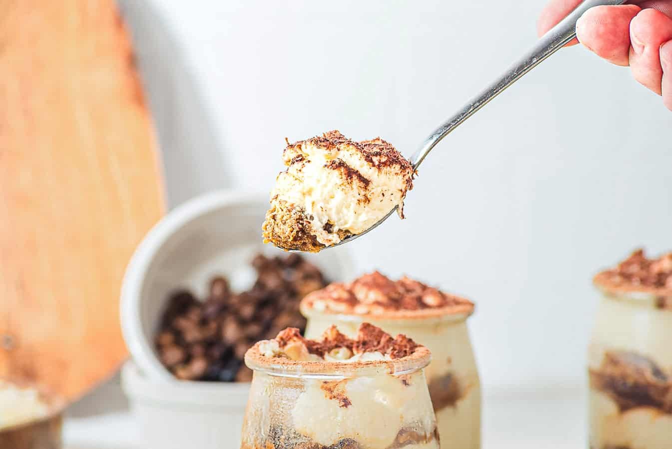 A spoonful of creamy dessert topped with cocoa held above jars of similar layered dessert.