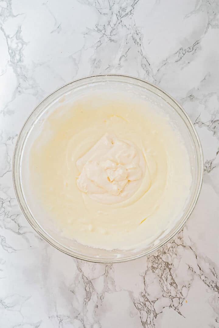 A glass bowl of creamy, whipped mixture on a white marble surface, seen from above.