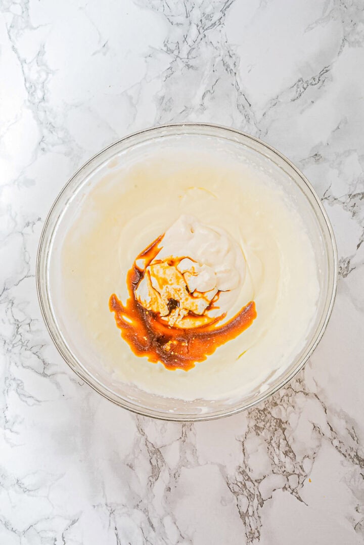 A glass bowl with creamy batter and swirls of vanilla extract on a marble countertop.