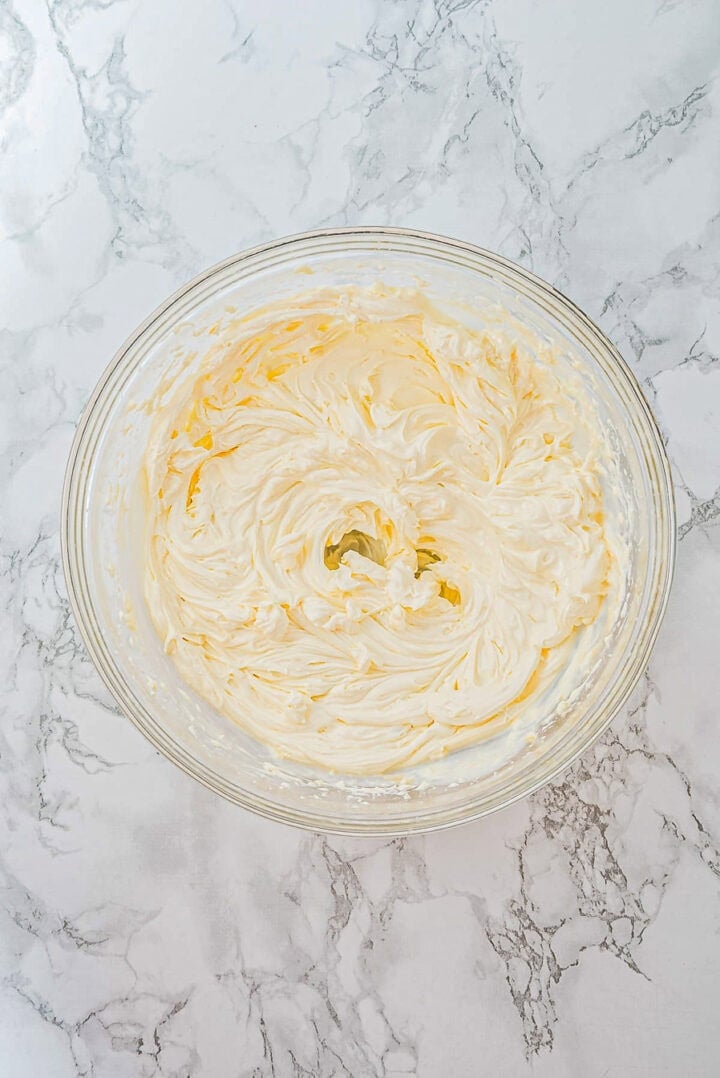 A glass bowl filled with whipped, creamy butter on a marble countertop.