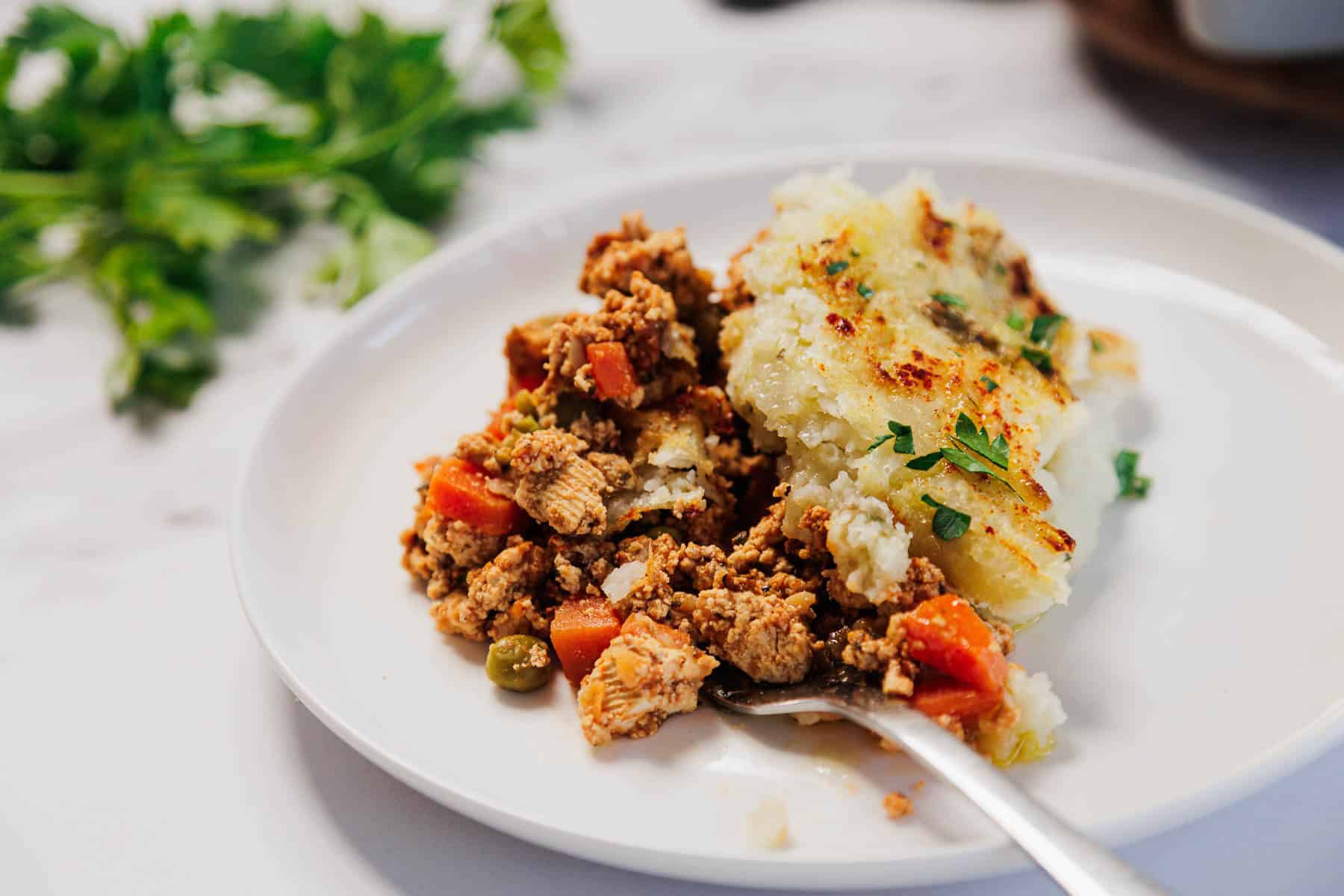 A plate of Vegetarian Shepherd's Pie with savory vegetables and creamy mashed potato topping, garnished with parsley.