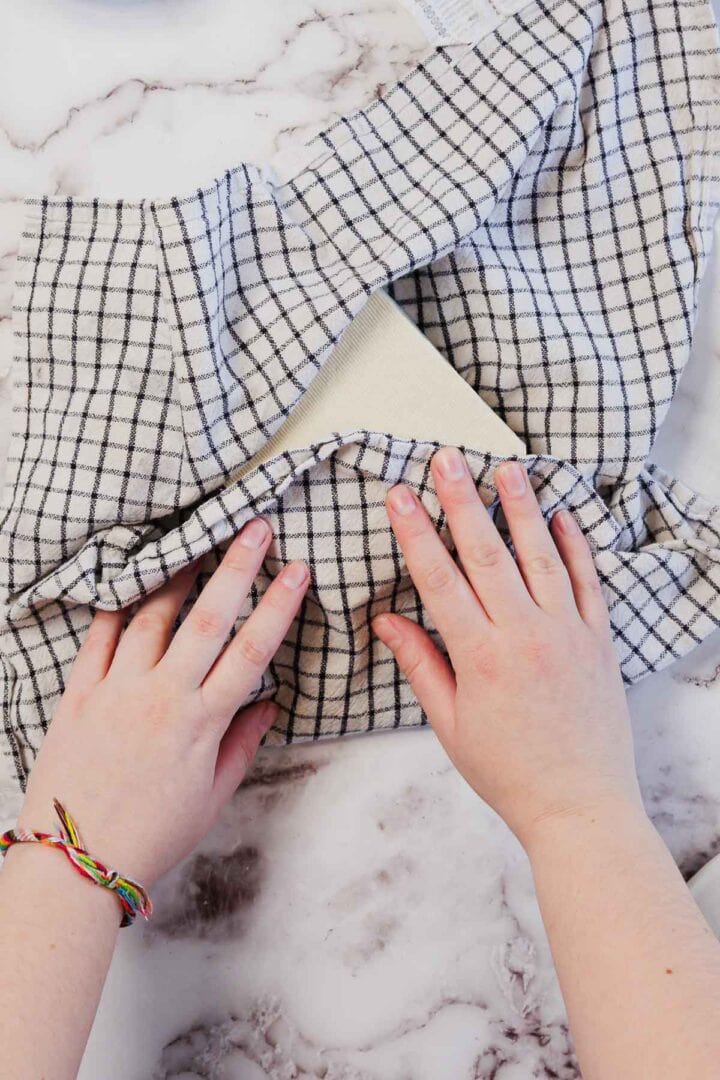Hands wrapping a block of tofu in a checkered cloth on a marble countertop, preparing the perfect base for a hearty Vegetarian Shepherd's Pie.