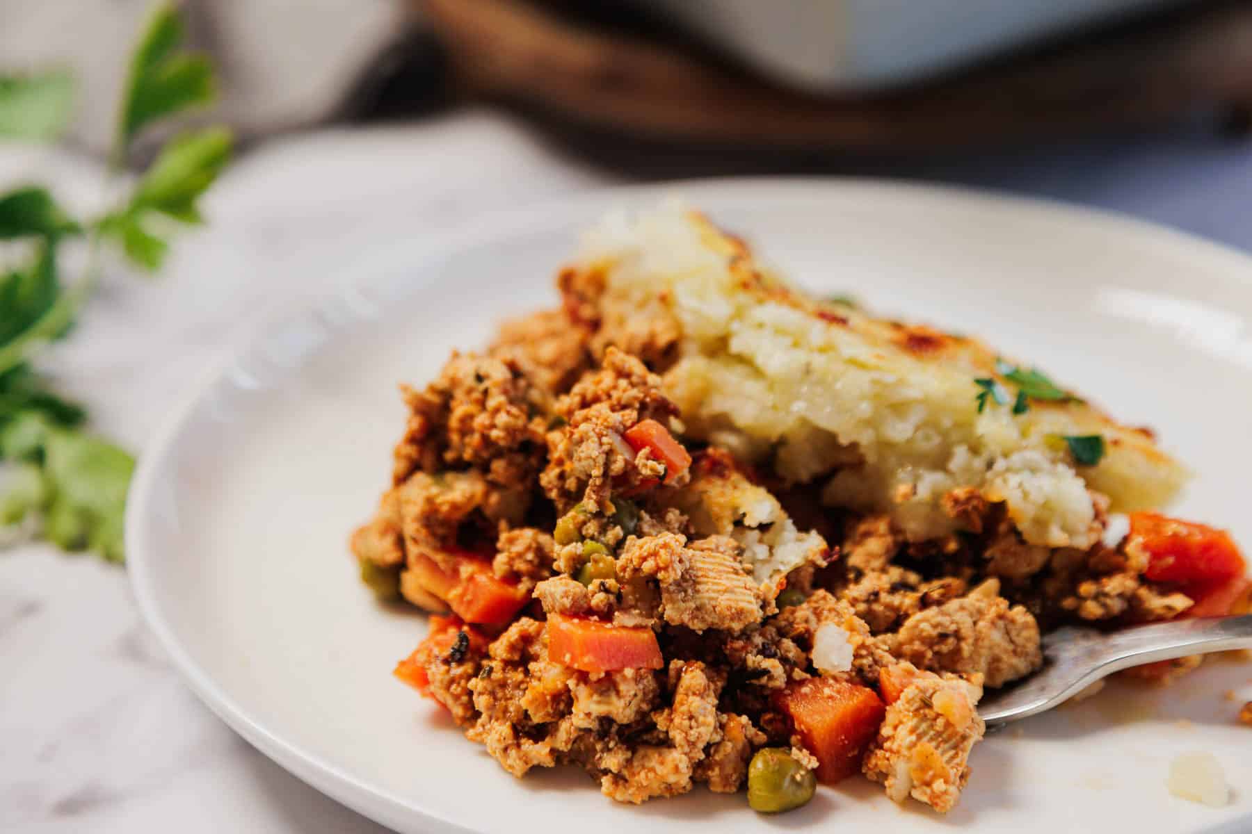 A serving of Vegetarian Shepherd's Pie with peas, carrots, and creamy mashed potatoes on a white plate.