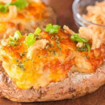 Baked potatoes topped with melted cheese, green onions, and crispy fried onions on a wooden surface.