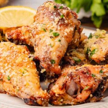 A plate of crispy garlic parmesan chicken wings garnished with herbs and served with lemon wedges.