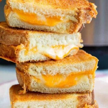 Stack of three grilled cheese sandwiches with melted cheese on a white plate, perfect for kid-friendly recipes.