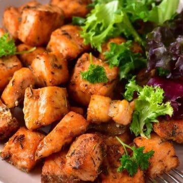 Grilled salmon cubes with fresh mixed greens on a white plate.