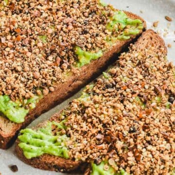 Two slices of toast topped with mashed avocado and sprinkled with mixed seeds on a plate.