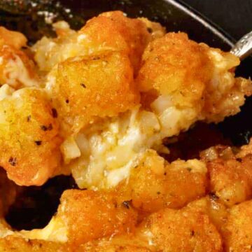 A close-up of cheesy tater tot casserole being served from a skillet with a spoon.