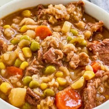 A bowl of hearty beef and vegetable soup with carrots, corn, peas, and chunks of beef.