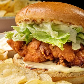 A crispy fried chicken sandwich with lettuce and mayo, served with a side of potato chips.
